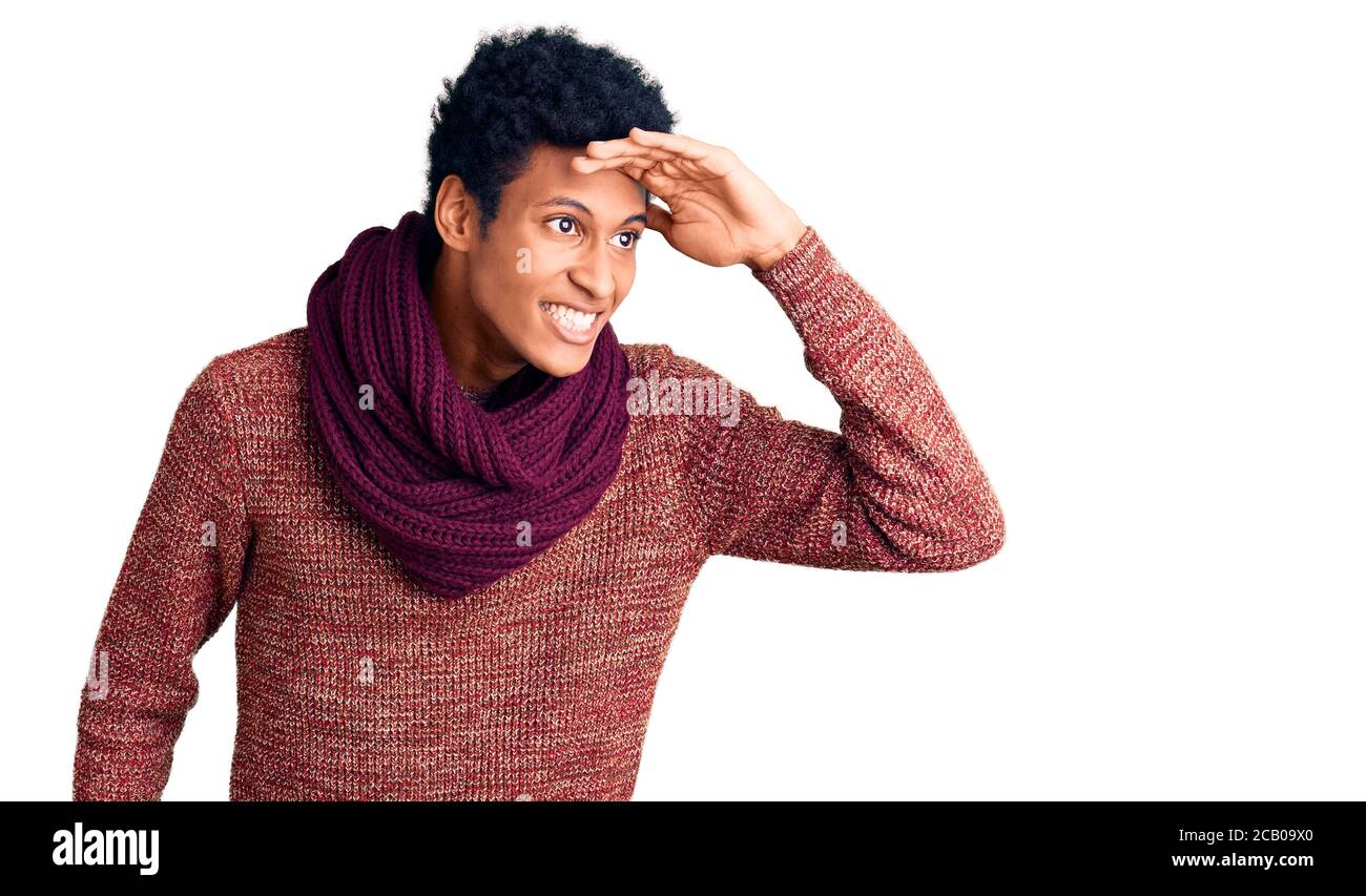 Jeune afro-américain vêtu d'un chandail et d'une écharpe d'hiver décontractés très heureux et souriants regardant loin avec la main sur la tête. Concept de recherche. Banque D'Images