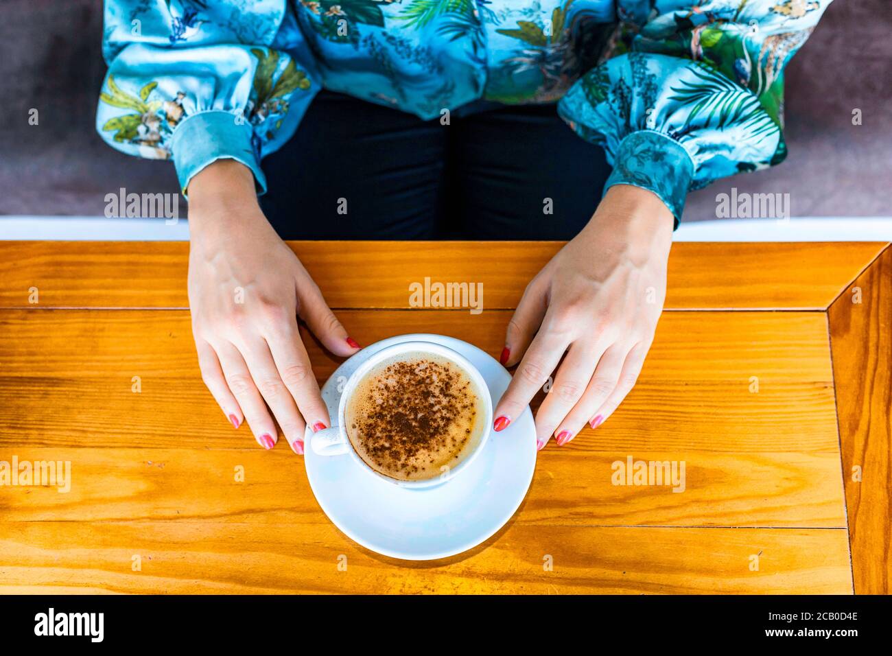 Vue du dessus des deux mains d'une femme avec vernis à ongles rouge tout en buvant un cappuccino dans un Café local à Lisbonne Banque D'Images
