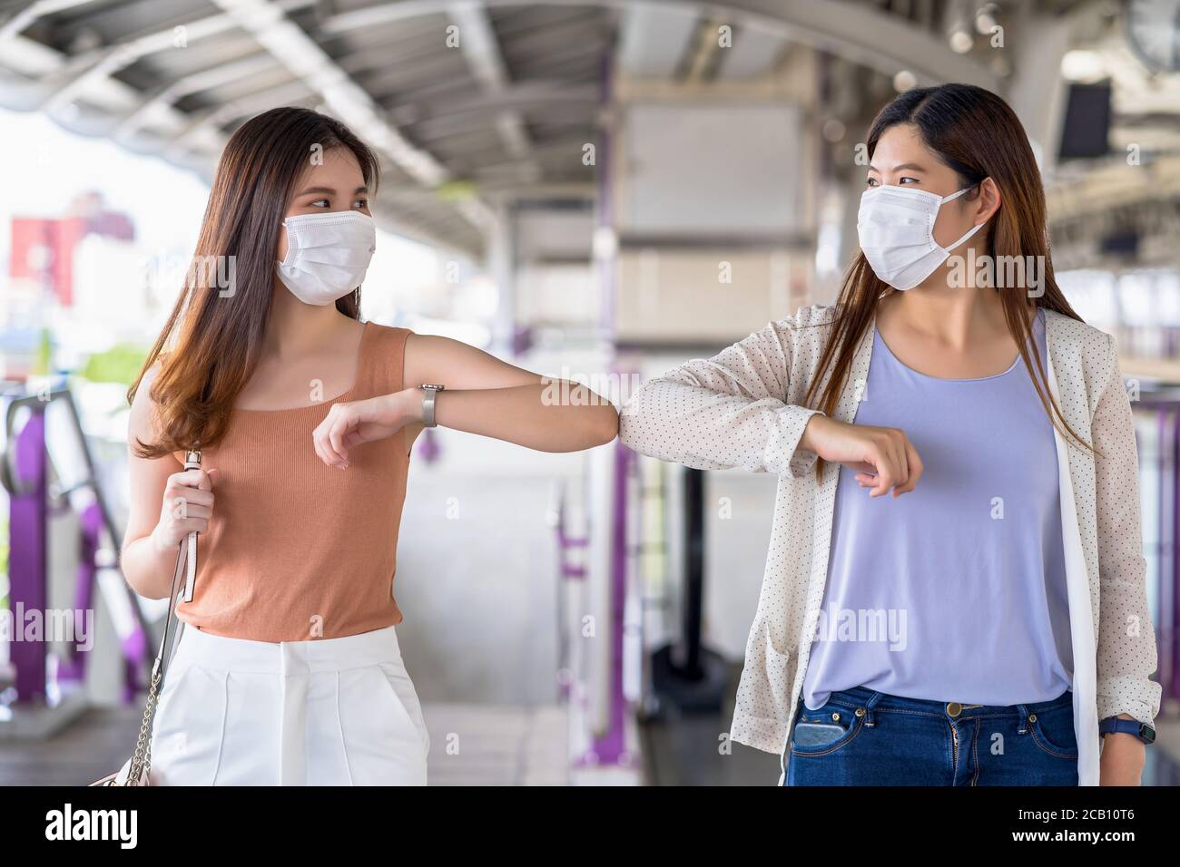 Une jeune femme asiatique, passager portant un masque chirurgical et des coudes, se heurte à un ami dans un train de métro lors d'un voyage dans la grande ville à l'épidémie de Covid19, Banque D'Images