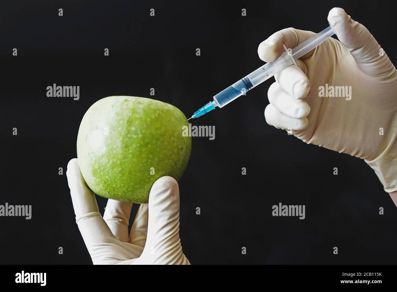 Une seringue est coincée dans une pomme dans la main sur fond noir. Concept de légumes et de fruits génétiquement modifiés Banque D'Images