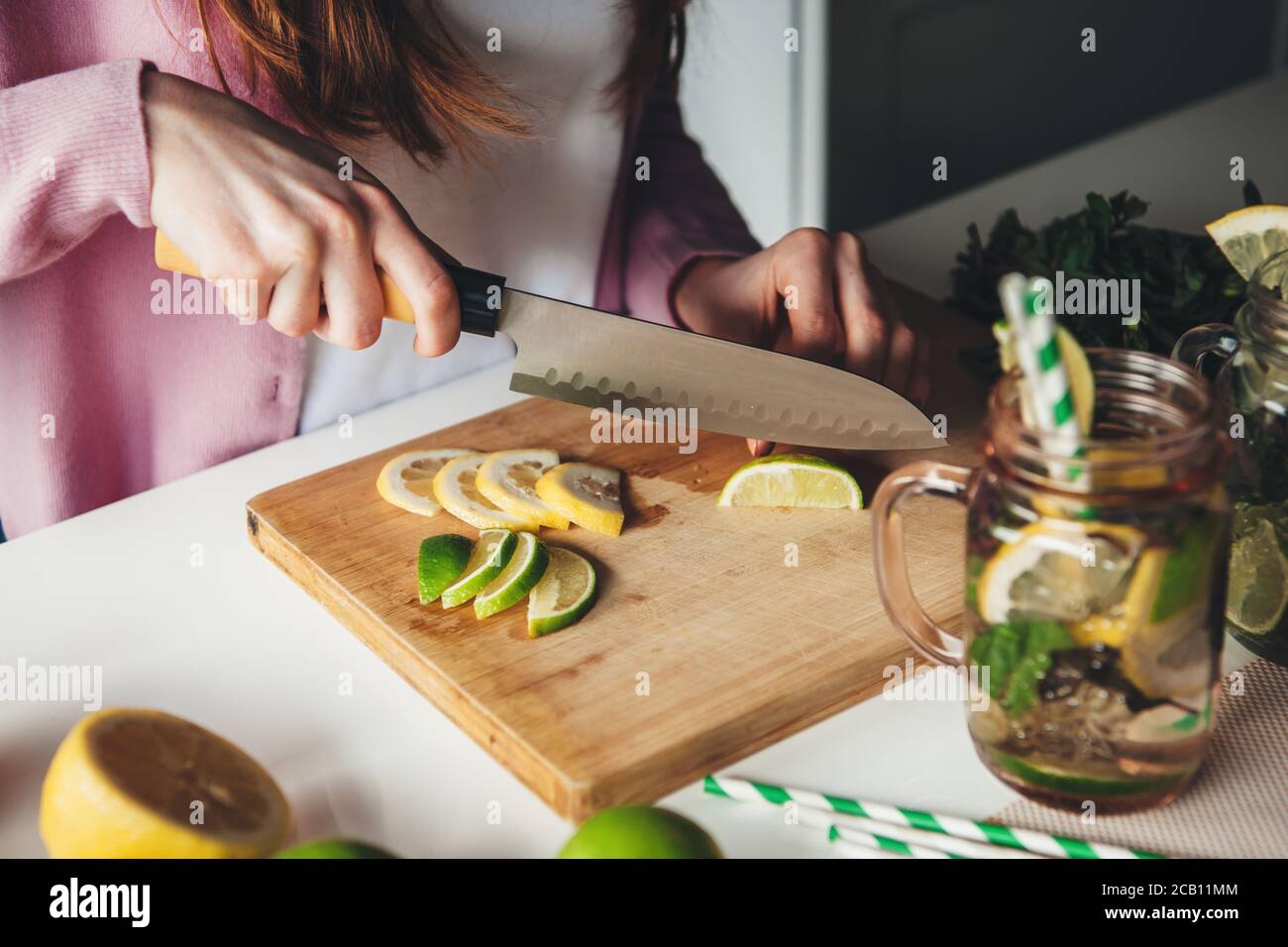 Photo vue latérale d'une dame de gingembre préparant mojito à à la maison, trancher le citron avec un couteau Banque D'Images