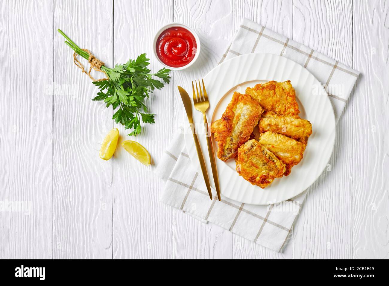 Filet de morue beurré de style britannique poêlé, servi sur une assiette blanche avec couverts, ketchup de tomate, persil frais sur fond de bois blanc, Top vie Banque D'Images