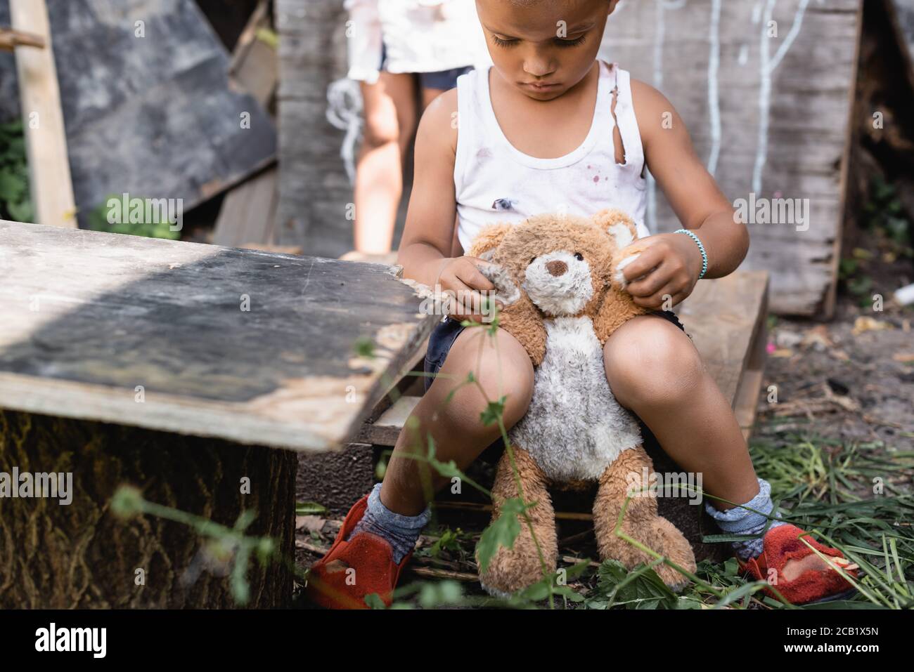 attention sélective aux enfants pauvres d'afrique-amérique dans des vêtements déchirés assis avec un jouet doux Banque D'Images