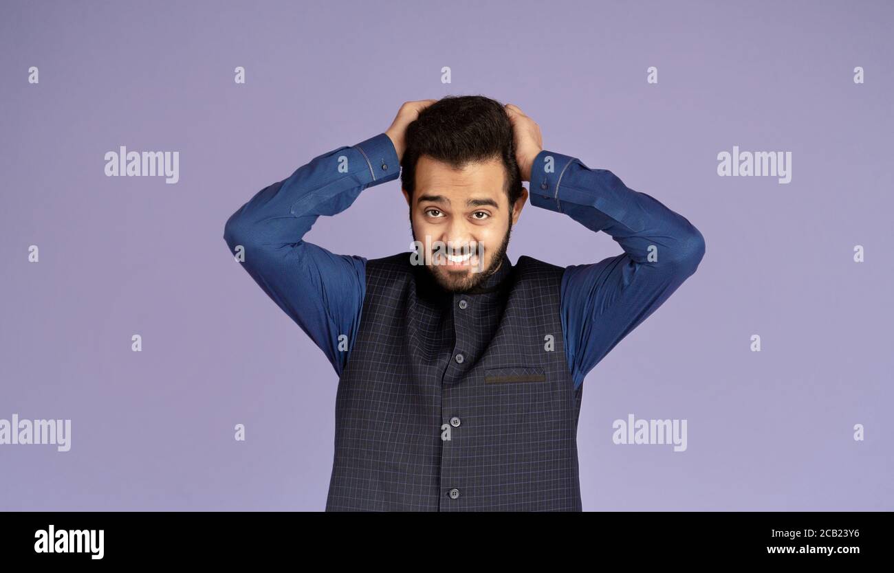 Homme indien émotionnel tirant les cheveux dans le désespoir sur fond violet Banque D'Images