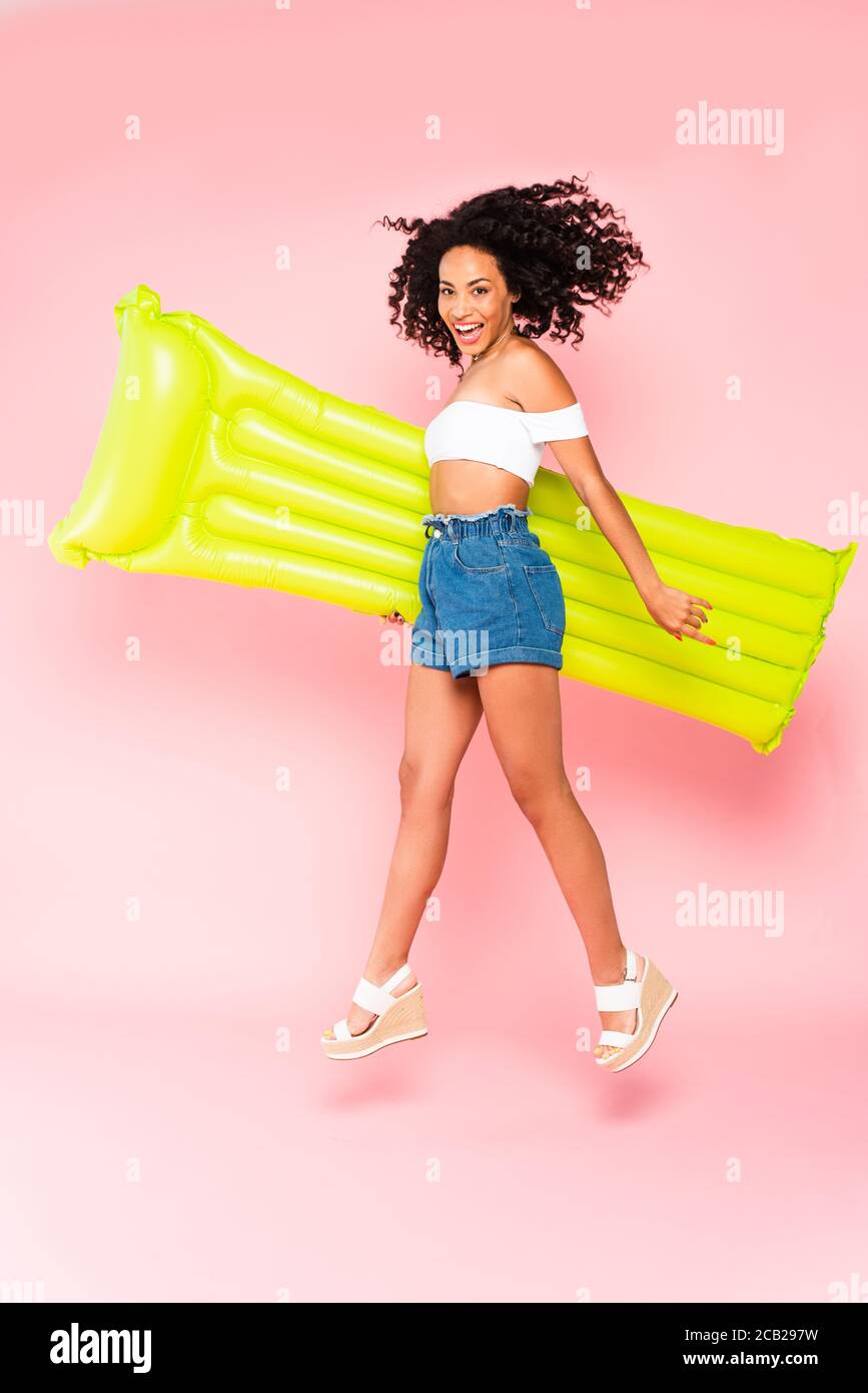 bonne fille afro-américaine sautant avec matelas gonflable sur rose Banque D'Images
