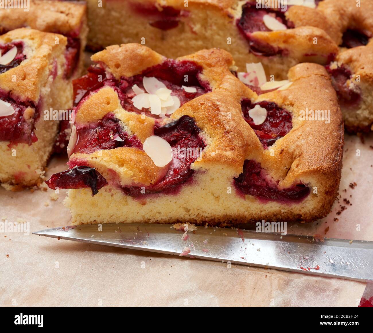 des tranches de gâteau de savoie cuites avec des prunes sur du papier brun et un couteau, gros plan Banque D'Images