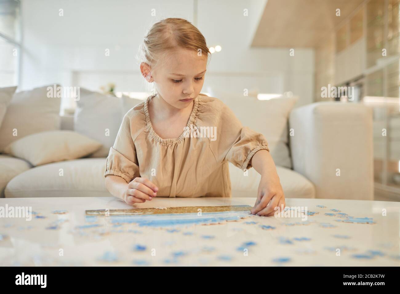 Portrait aux tons chauds d'une petite fille à la résolution de puzzle puzzle tout en appréciant le temps à l'intérieur à la maison, l'espace de copie Banque D'Images