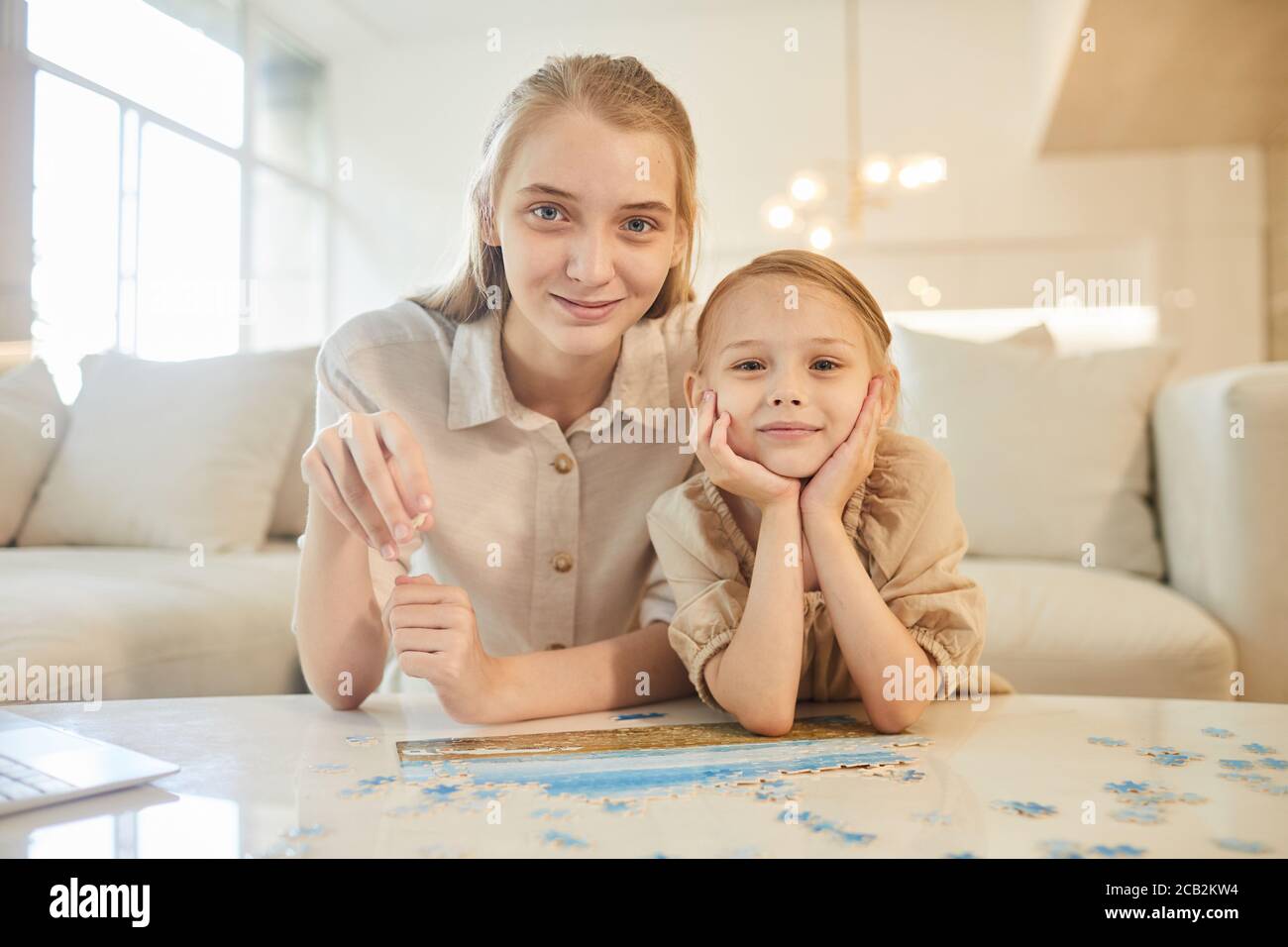 Portrait aux tons chauds de deux sœurs qui se réunissent pour résoudre des énigmes tout en appréciant le temps à l'intérieur à la maison et en regardant l'appareil photo, l'espace de copie Banque D'Images