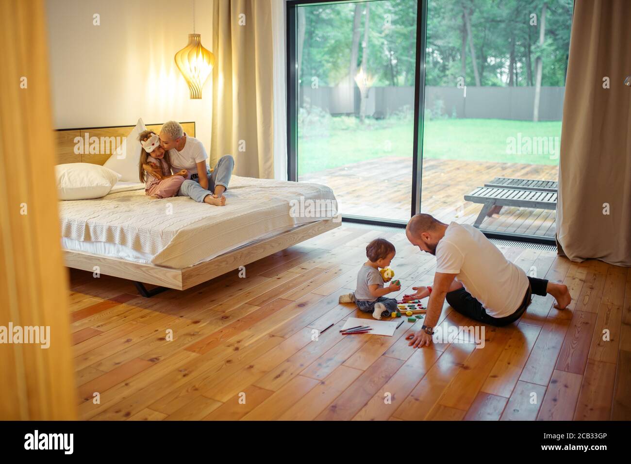Mère et fille assise sur le lit, maman embrassant l'enfant. Père avec son fils jouant sur le sol. Concept de famille Banque D'Images