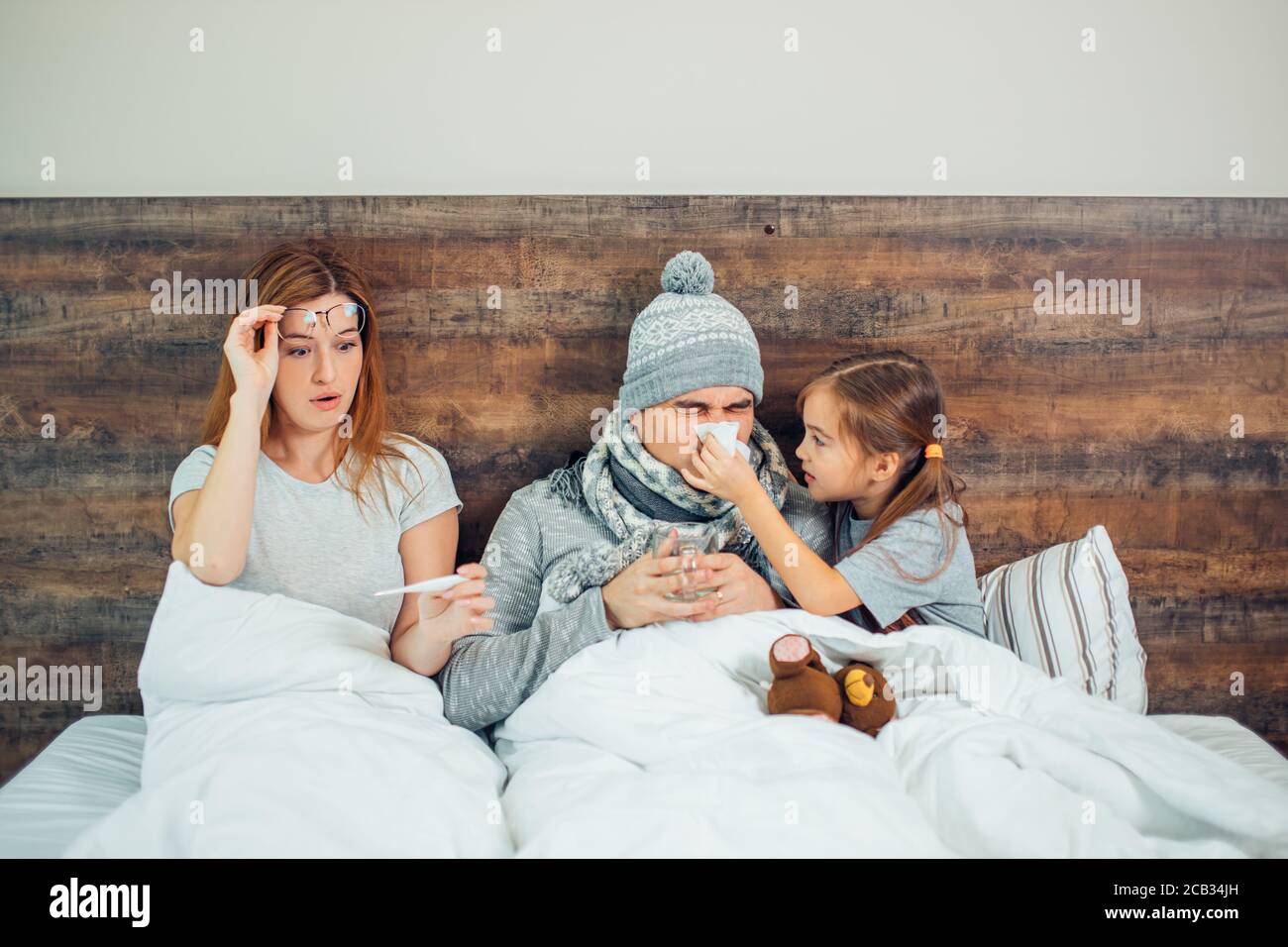 famille caucasienne malade, couchée au lit ensemble, souffrant de maladie. Un homme, une femme et une fille malsains se traitant à la maison Banque D'Images