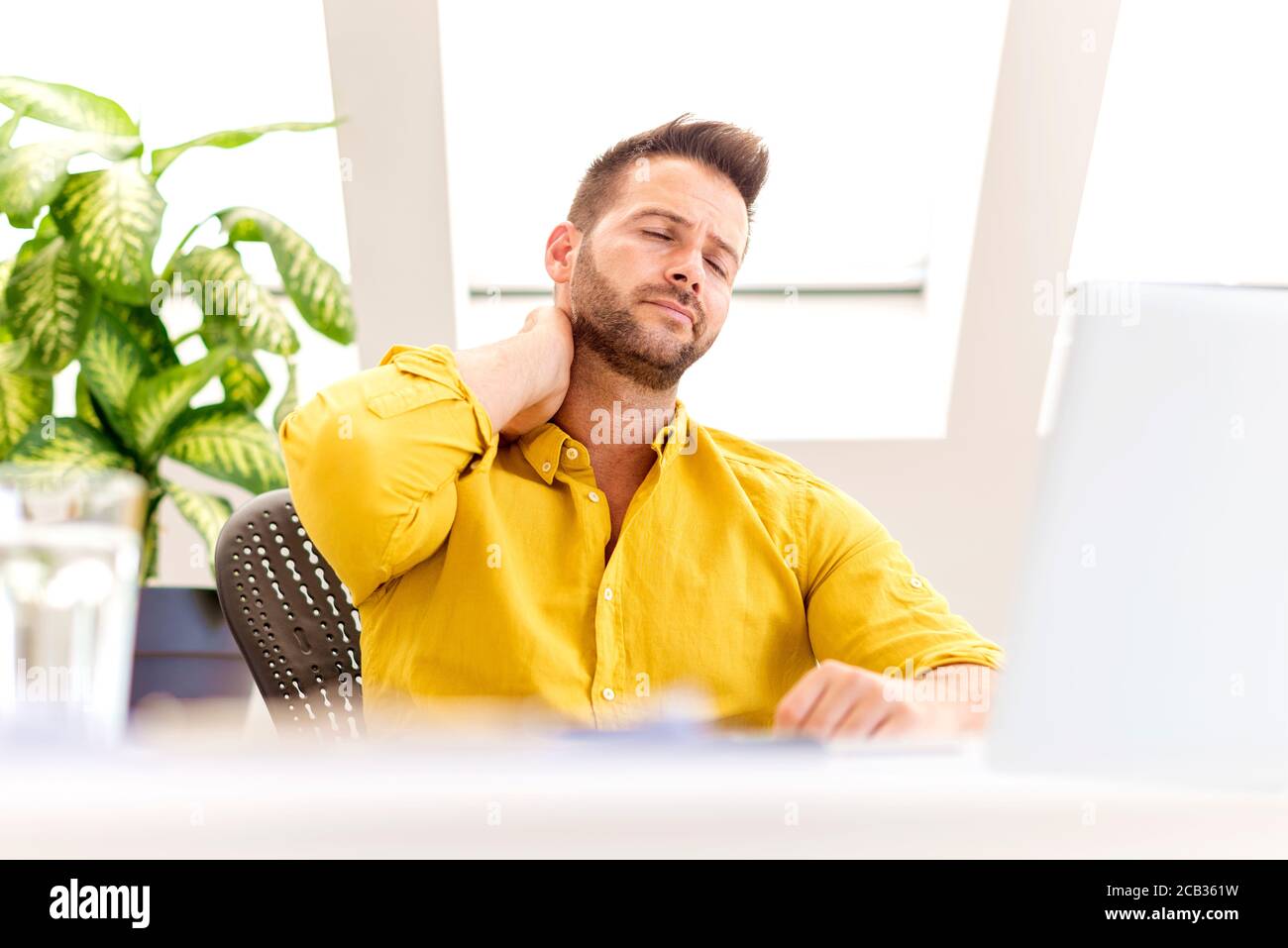 Photo d'un homme d'affaires stressant assis derrière son ordinateur portable et souffrant d'une forte douleur à la tête. Banque D'Images