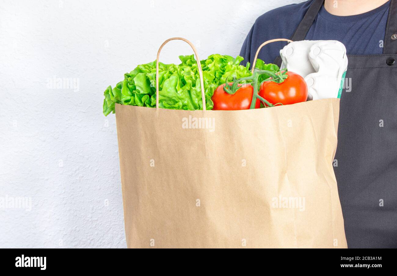 Homme tenant un sac en papier avec de la laitue, de la tomate et une boîte d'œufs sur fond blanc. Banque D'Images