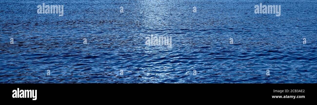 De petites vagues d'eau se déplacent dans la mer. Texture ou arrière-plan. Soleil en soirée dans l'eau de mer bleue. Longue bannière tendance en couleur de l'année 2020 Banque D'Images