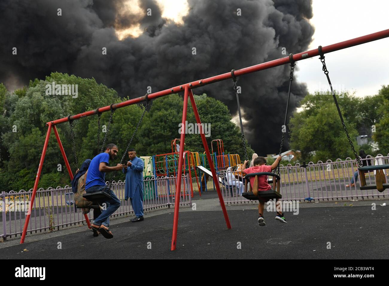 Les gens dans un parc comme la fumée se blère d'un incendie grave sur un domaine industriel à Birmingham. Les équipes de 10 moteurs d'incendie s'attaquent à l'incendie. Banque D'Images