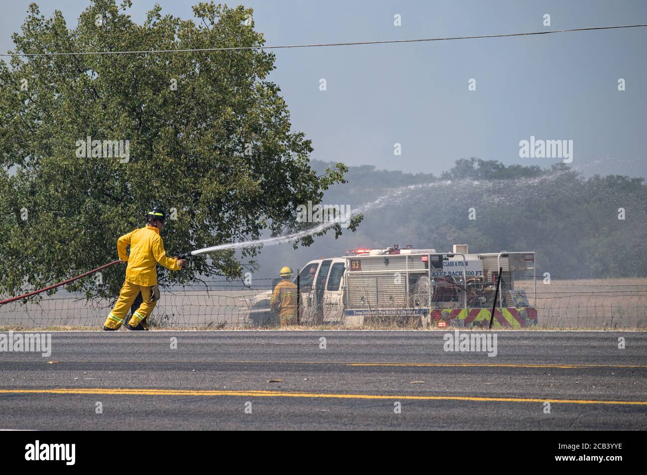 Brownwood, Texas USA-août 10 2020: Camions d'incendie moteurs les combattants éteignent un feu de forêt brumeux sur le bord de la route causé par la litière de cigarette allumée par la sécheresse. Banque D'Images