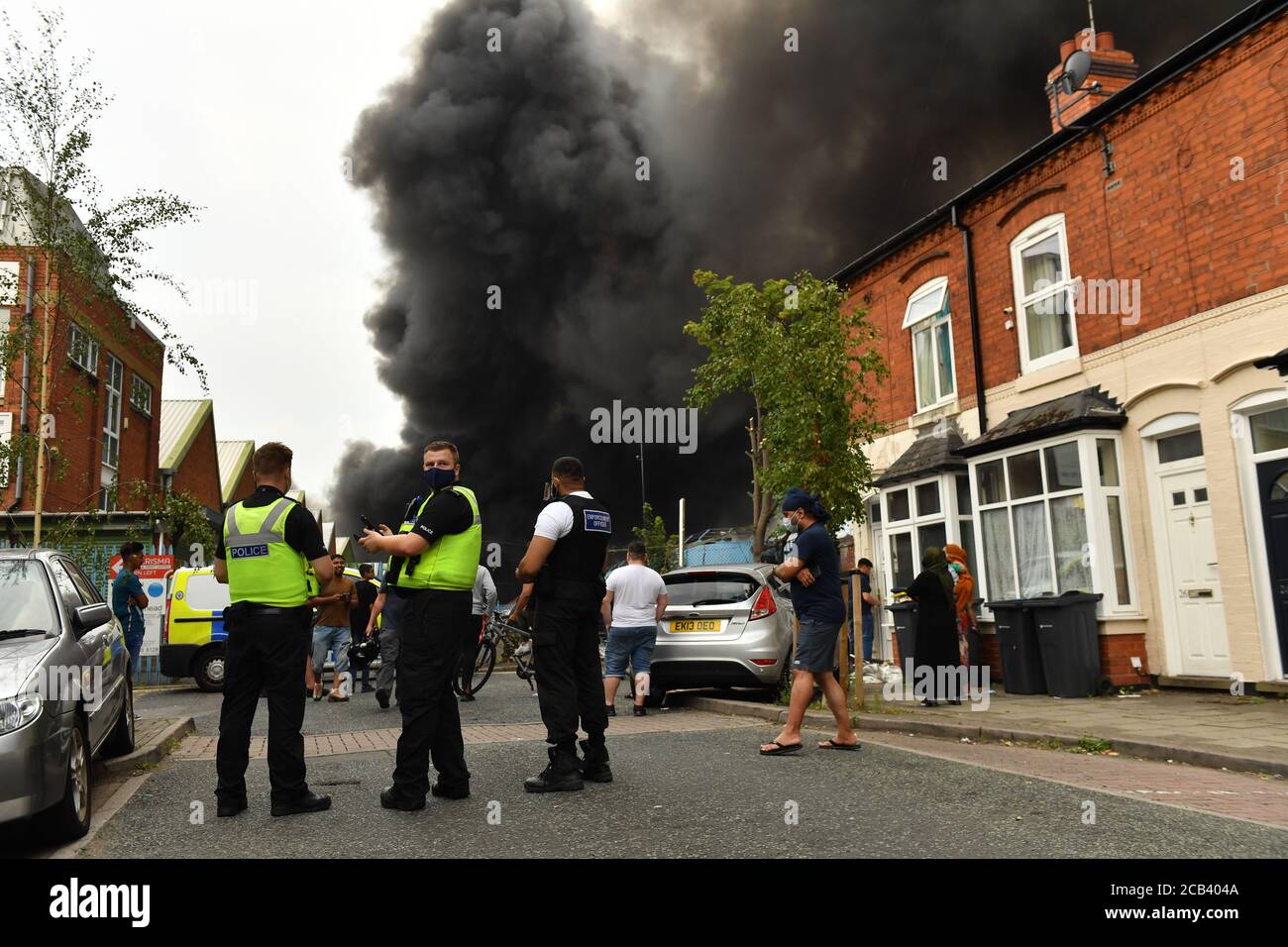 La police et les habitants de la région observent le fait que de la fumée s'échappe d'un incendie violent dans une zone industrielle de Birmingham. Les équipes de 10 moteurs d'incendie s'attaquent à l'incendie. Banque D'Images