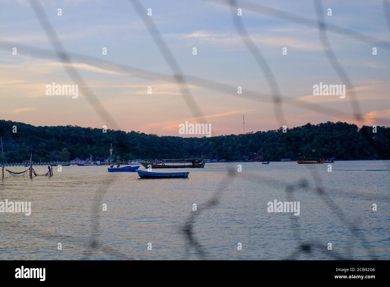 Île de Koh Rong Samloem, baie de Saracen, Cambodge, Asie du Sud-est. Bateaux sur l'eau au coucher du soleil. Jeu de focus à travers un résille placé sur la plage. Banque D'Images