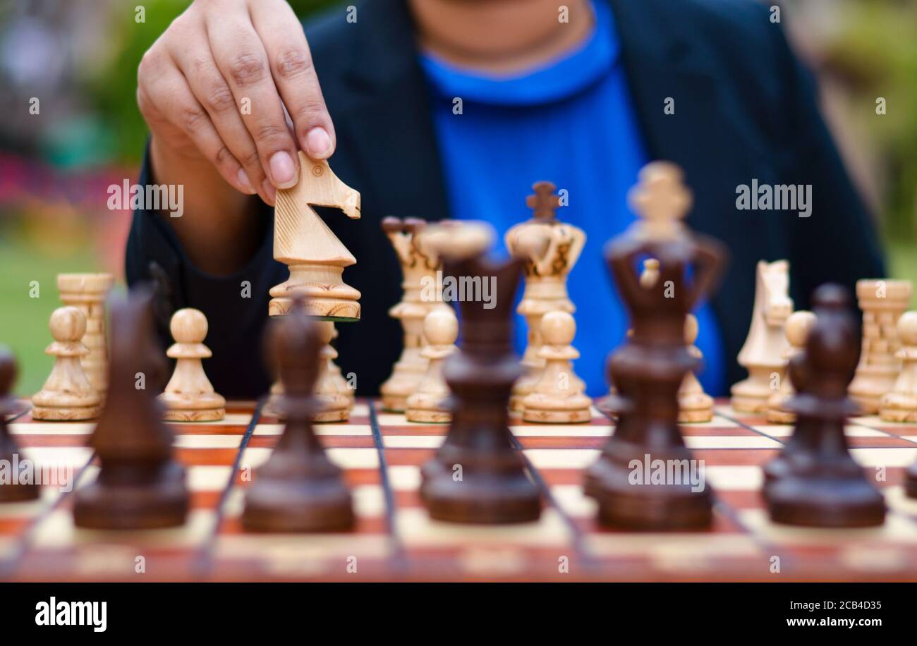 Une fille jouant aux échecs en déplaçant le chevalier blanc vers l'avant sur un plateau d'échecs avec le chevalier choisi dans ses mains. Concept - idée, stratégie Banque D'Images