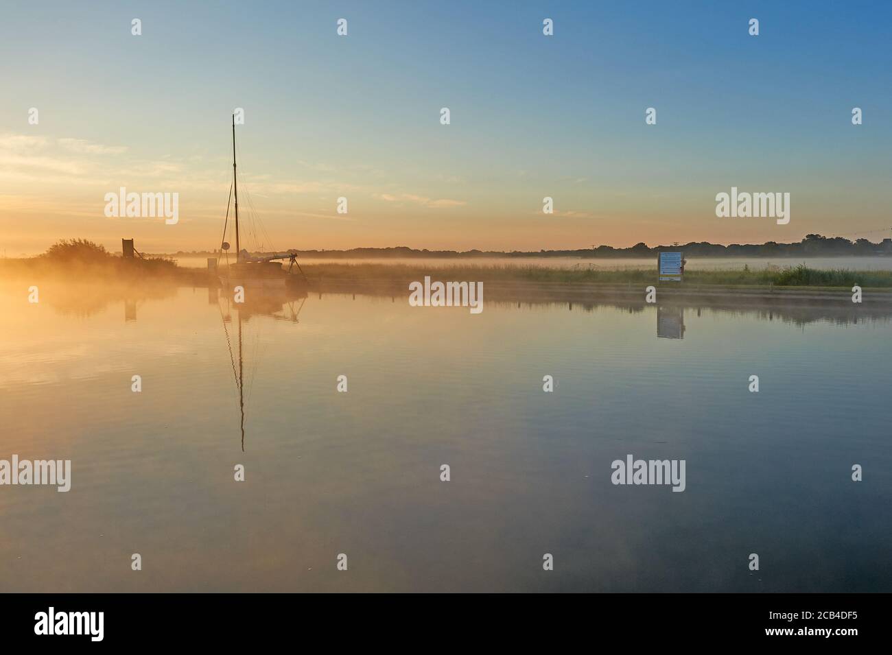 Potter Heigham, Norfolk Broads et un voilier amarré sur la rivière Thurne pendant un lever de soleil brumeux d'été. Banque D'Images