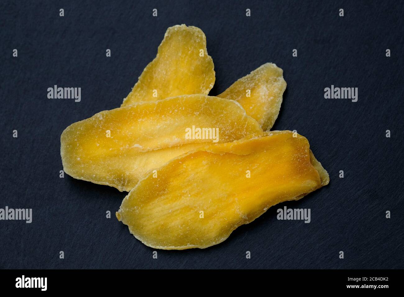 Mangue séchée sans sucre. Pétales de mangue naturelle sur un tableau noir vue du dessus. Pulpe de mangue séchée, fruits secs, collations végétariennes saines. Banque D'Images