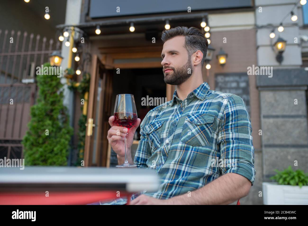 Beau homme barbu assis dans un café en plein air, en dégustant un verre de vin rouge Banque D'Images