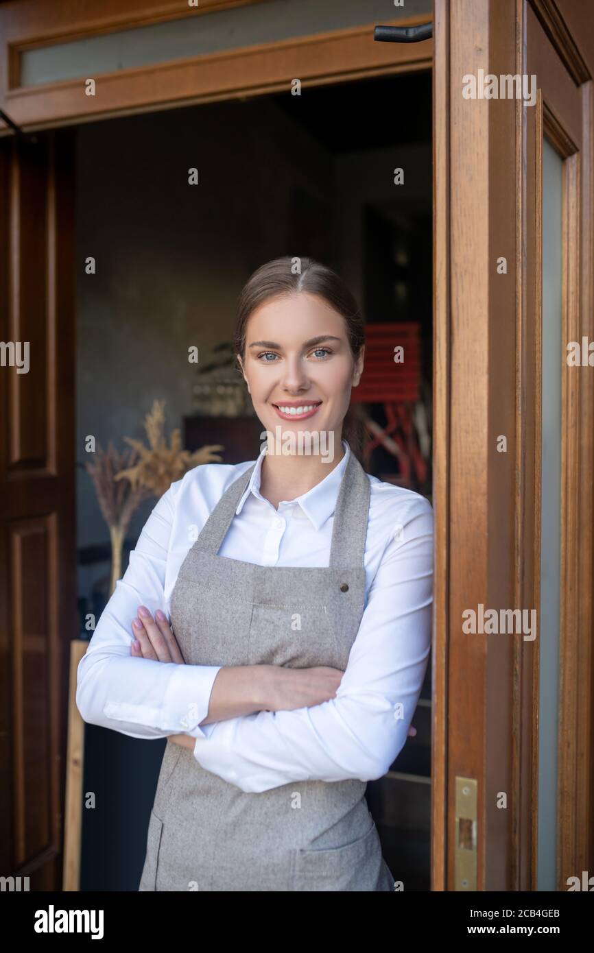 Charmante jeune serveuse penchée à la porte, croisant ses bras, souriant Banque D'Images