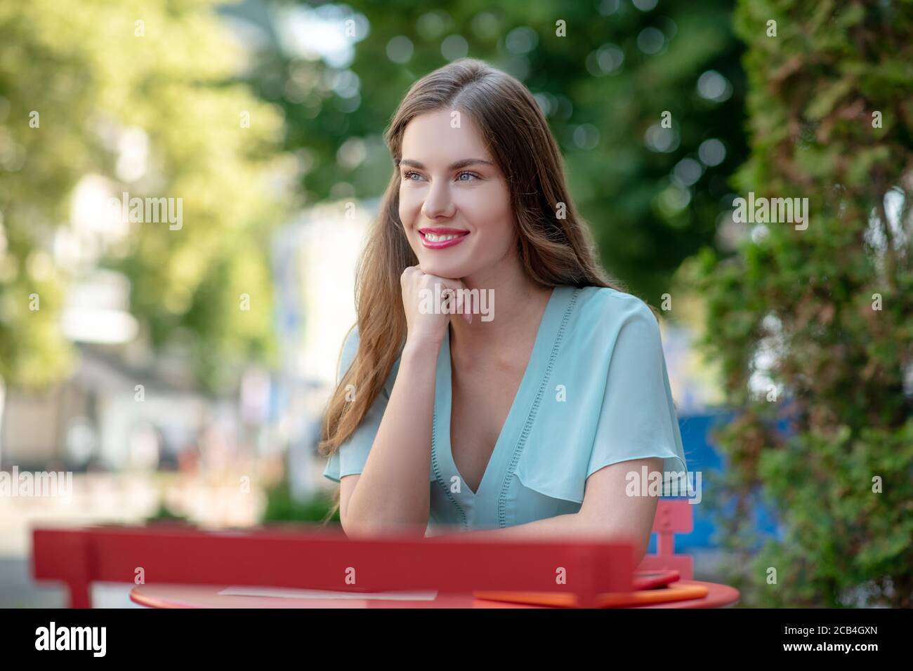 Femme romantique souriante assise au café, tenant sa main sous le menton Banque D'Images