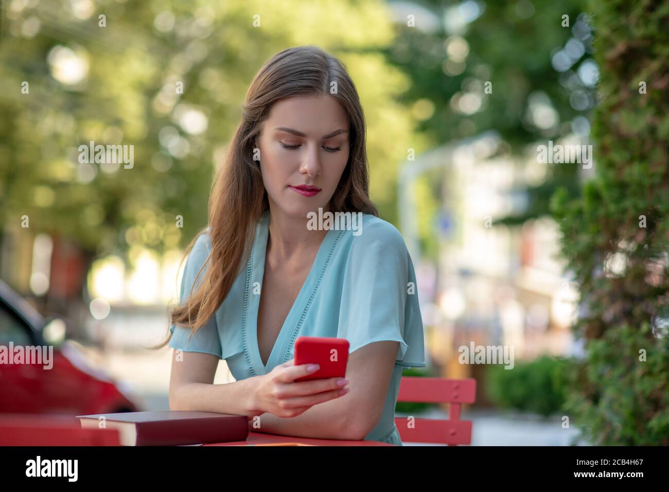 Contrarié femme assis dans un café, vérifiant le téléphone, piquant les lèvres Banque D'Images