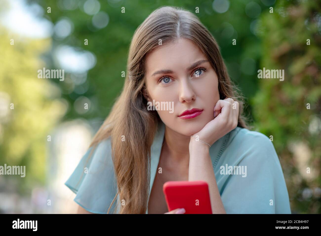 S'ennuient une jolie femme tenant son smartphone, en posant son menton à la main Banque D'Images