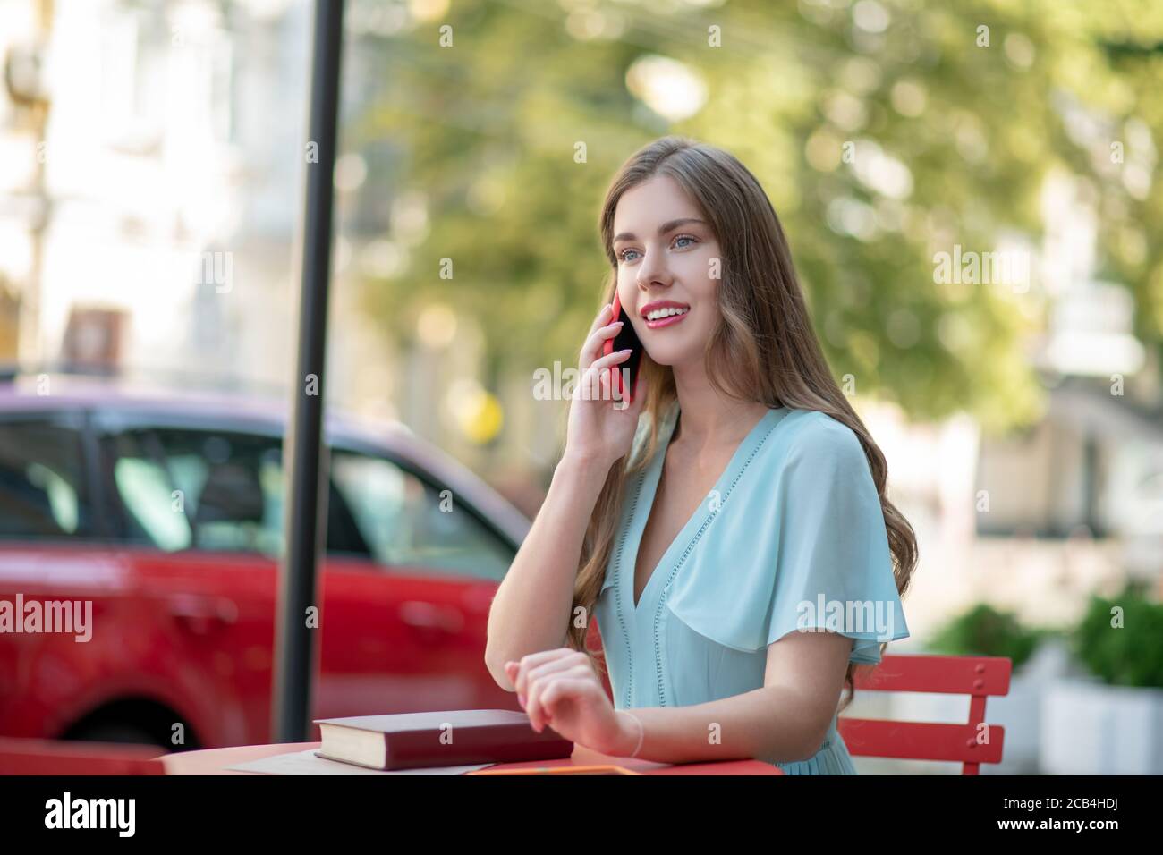 Femme romantique aux lèvres rouges assise dans un café en plein air, parlant au téléphone Banque D'Images