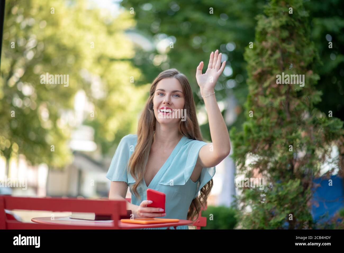 Femme romantique aux lèvres rouges assise dans un café en plein air, agitant sa main Banque D'Images