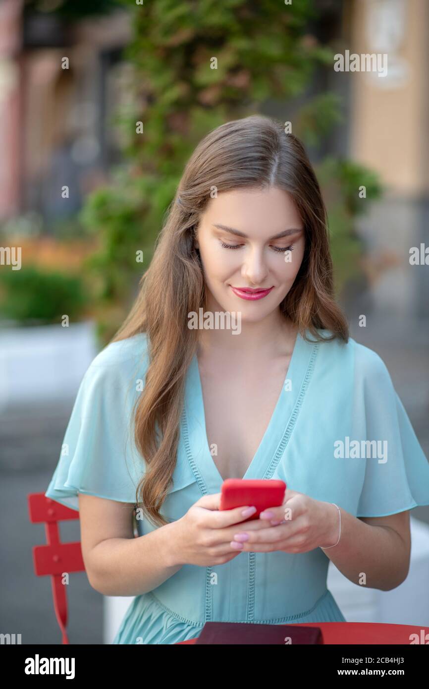 Femme romantique aux lèvres rouges assis dans un café en plein air, texto, souriant Banque D'Images