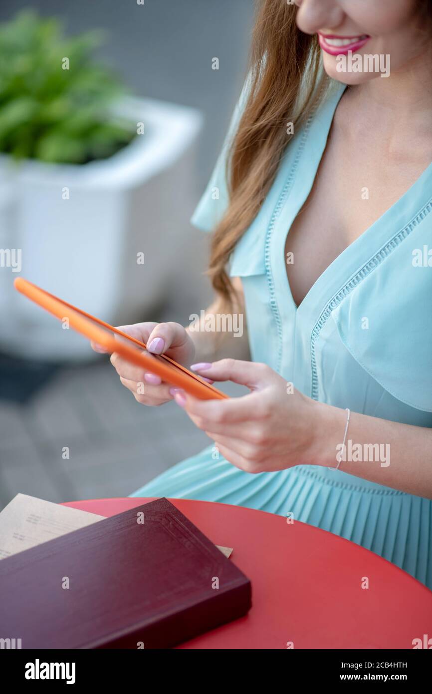 Gros plan des mains des femmes tenant la tablette orange au-dessus de la table avec livre Banque D'Images