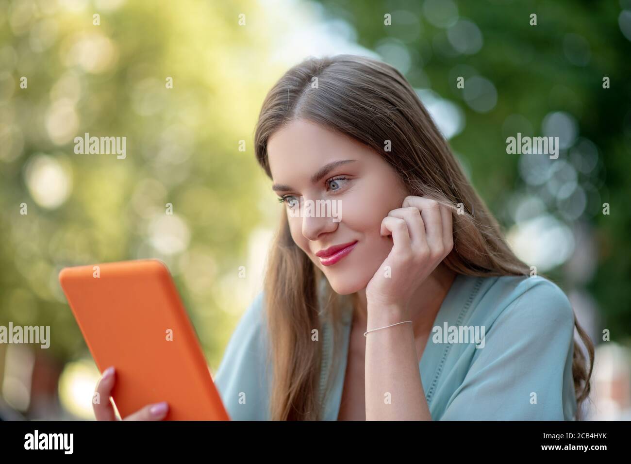 Femme romantique tenant une tablette orange, posant son menton sur sa main Banque D'Images