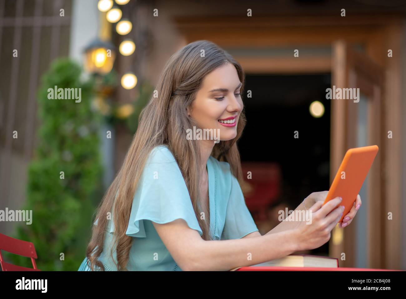 Femme romantique assise dans un café en plein air, avec une tablette orange Banque D'Images