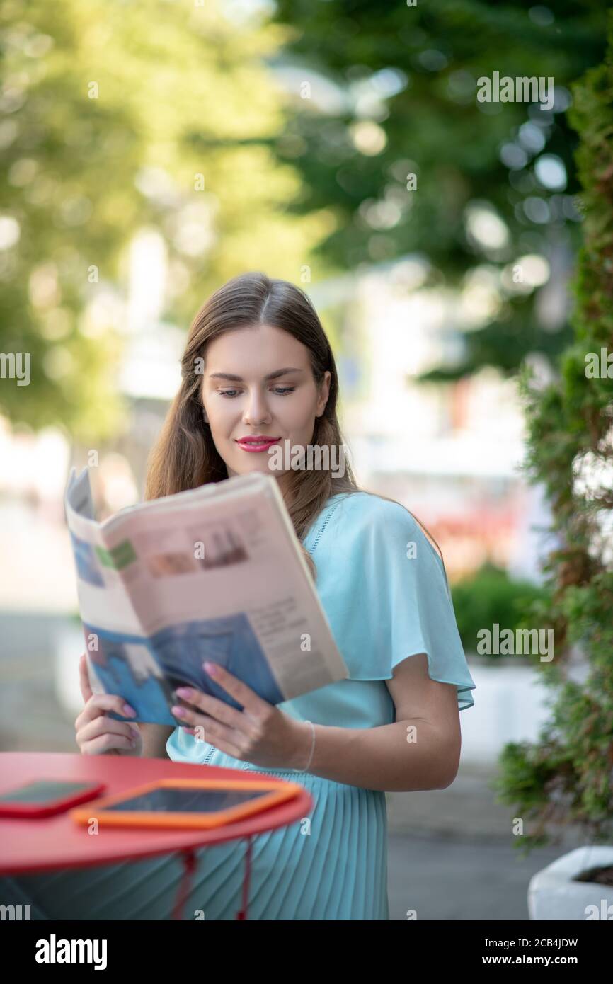 Charmante femme aux cheveux bruns qui lit dans un café, lisant des journaux Banque D'Images