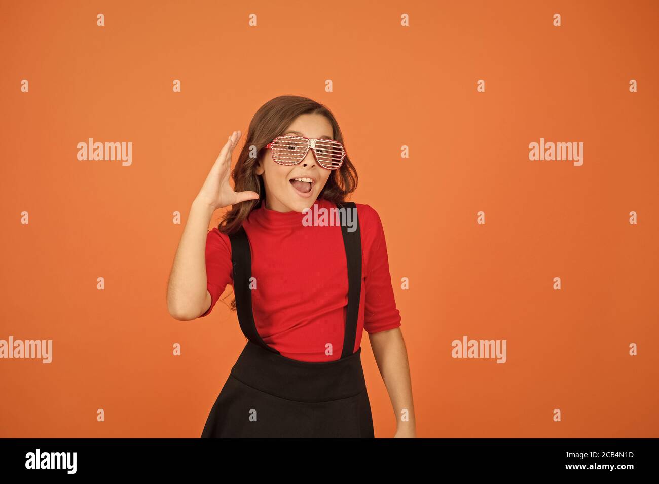 Je ne peux pas vous entendre. Joli et élégant enfant. bonne petite fille de l'uniforme scolaire. partie lunettes pour le plaisir. kid fashion concept. Restant concentré avec des lunettes. cool à élève fond orange. Banque D'Images