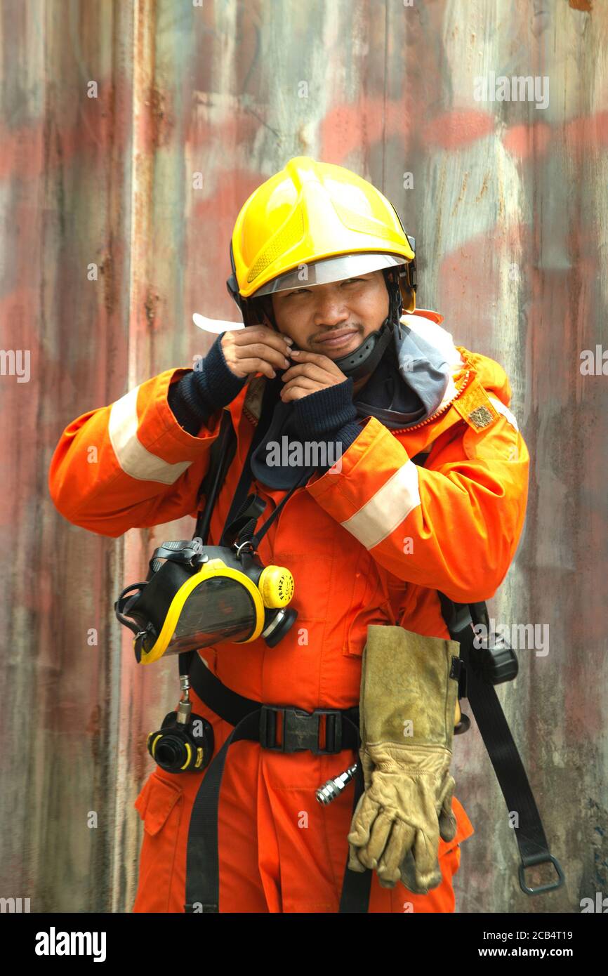 Le portrait des pompiers asiatiques porte un masque uniforme de protection contre le feu orange et la pose de casque se trouve devant le bâtiment. Banque D'Images