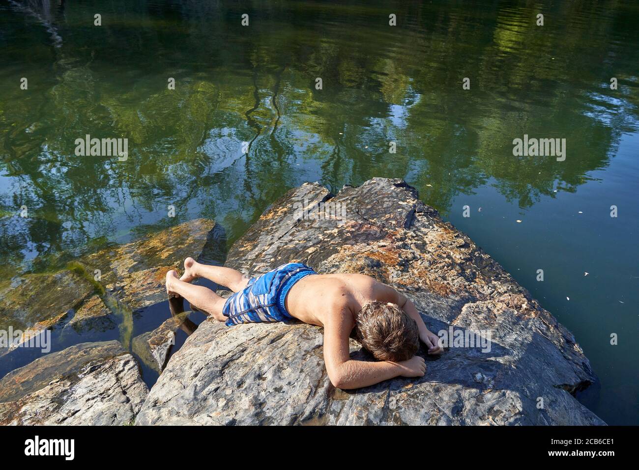 Un garçon qui se pose à l'estomac et prend un bain de soleil sur les rochers au bord de la rivière Russian près de Windsor dans le comté de Sonoma, Californie, États-Unis. Banque D'Images