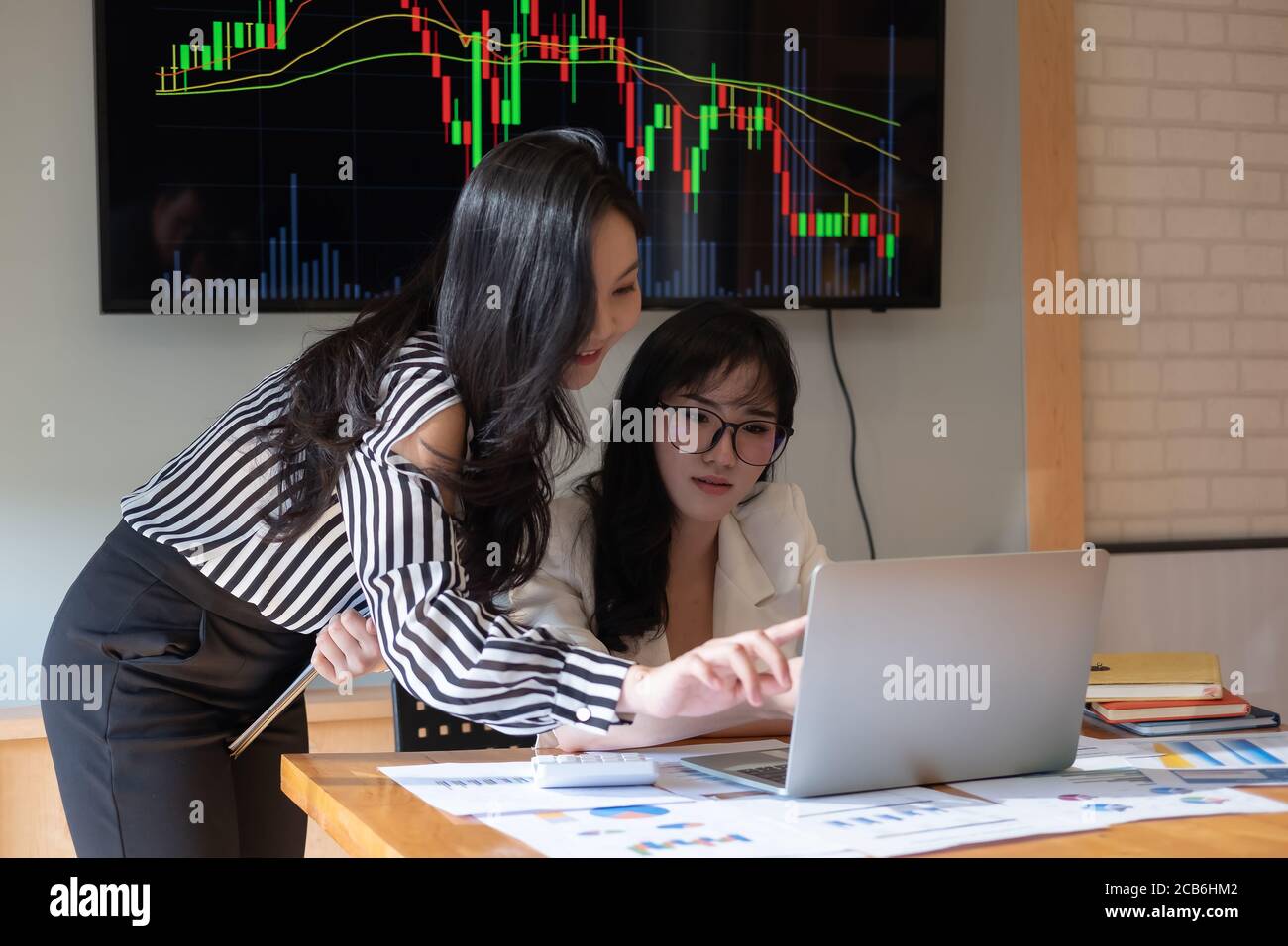 Des gens d'affaires se réunissent au bureau et discutent de documents, deux femmes avec un rapport financier avec un collègue partenaire sur ordinateur portable Banque D'Images