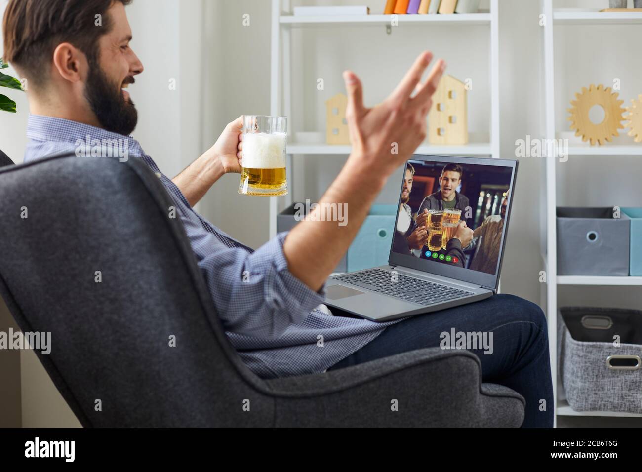 Fête virtuelle avec des amis en ligne. Un homme avec un verre de bière célèbre son anniversaire avec un groupe d'amis à distance à la maison. Banque D'Images