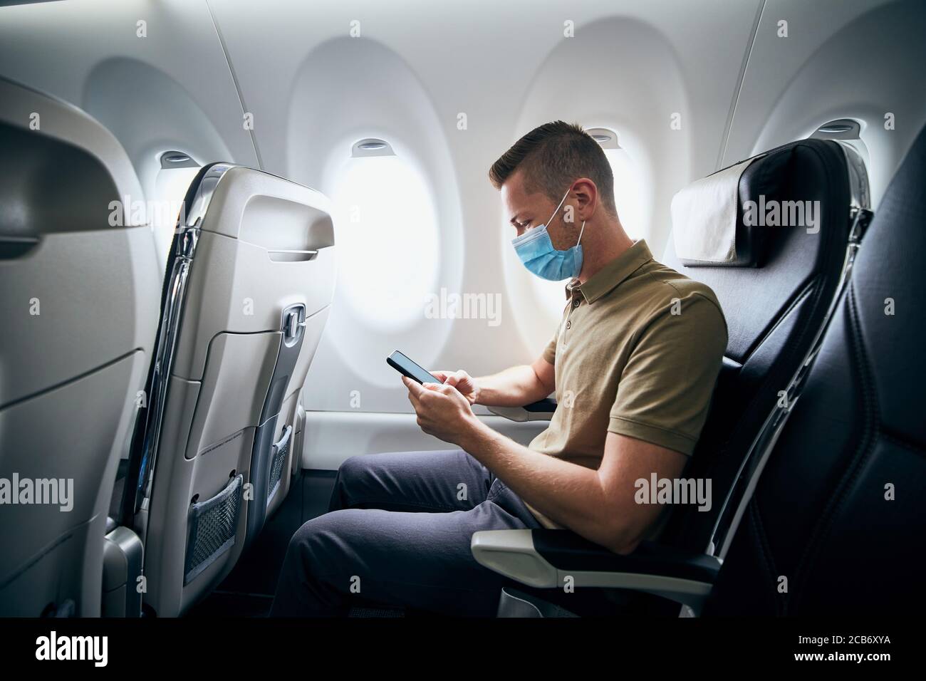 Homme portant un masque facial et utilisant le téléphone à l'intérieur de l'avion pendant le vol. Thèmes nouveau normal, coronavirus et protection personnelle. Banque D'Images