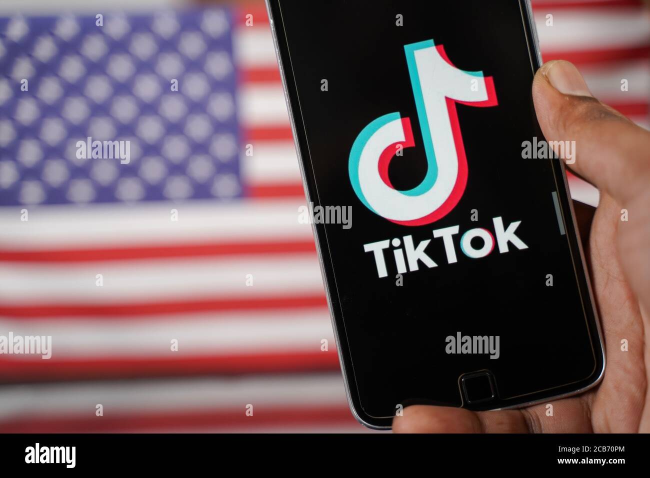 Maski, Inde - 4 août 2020 : gros plan des mains utilisant l'application tik tok avec drapeau américain ou américain comme arrière-plan et espace de copie. Banque D'Images