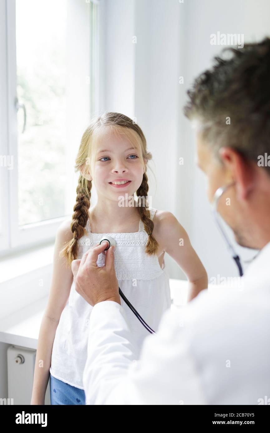 le médecin masculin en manteau blanc examine jeune, jolie fille dans sa pratique Banque D'Images