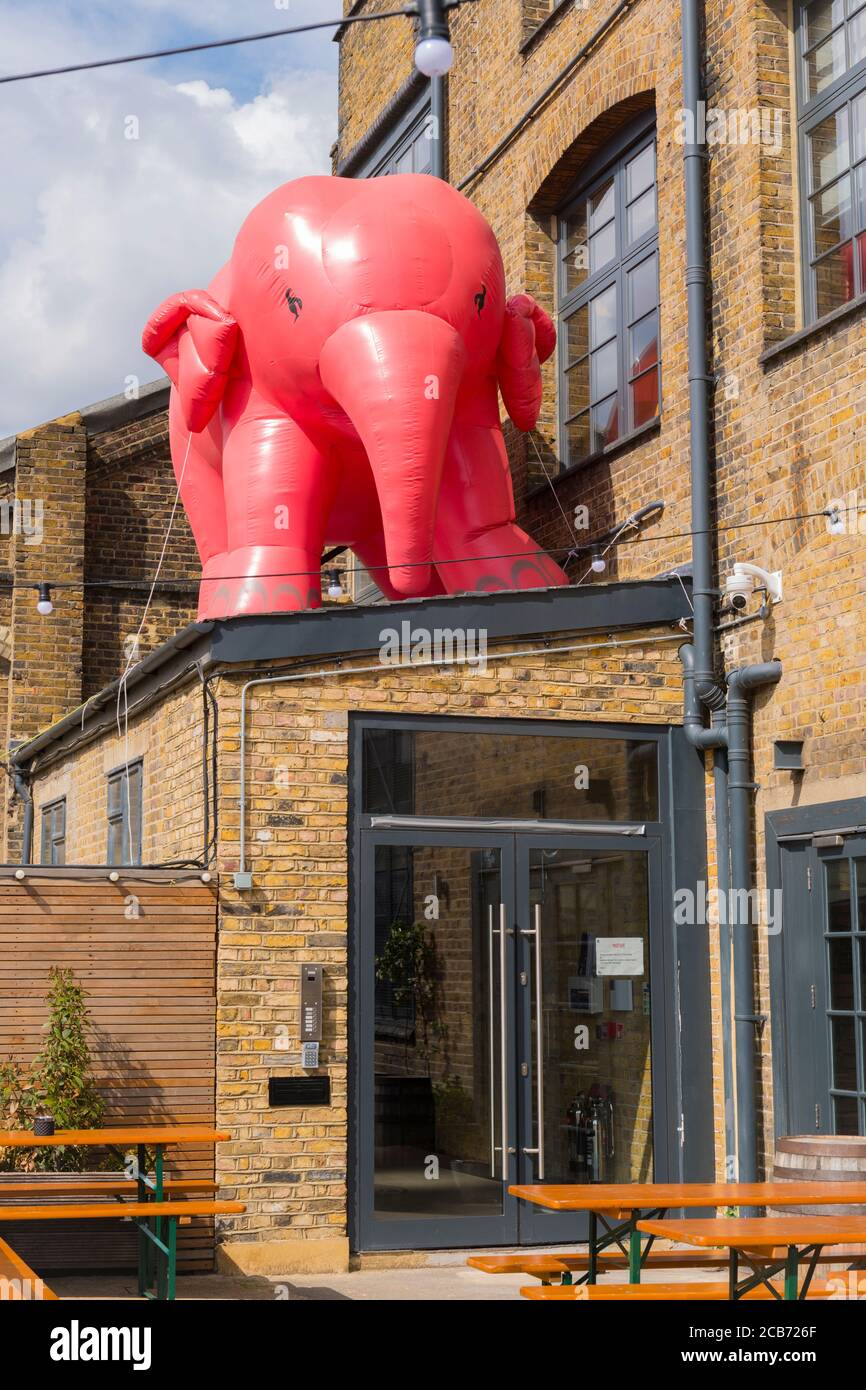 Angleterre London Stratford Park Hackney Wick éléphant rose gonflable géant au-dessus des portes vitrées d'entrée tables de bâtiment bancs drainpipe câbles fenêtres Banque D'Images