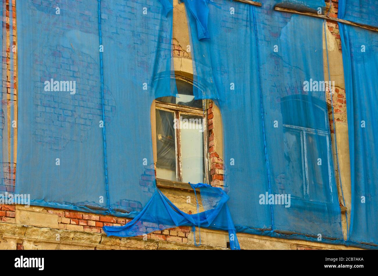 La façade d'un vieux bâtiment ruineux est tachetée des rideaux bleus pour protéger les piétons Banque D'Images