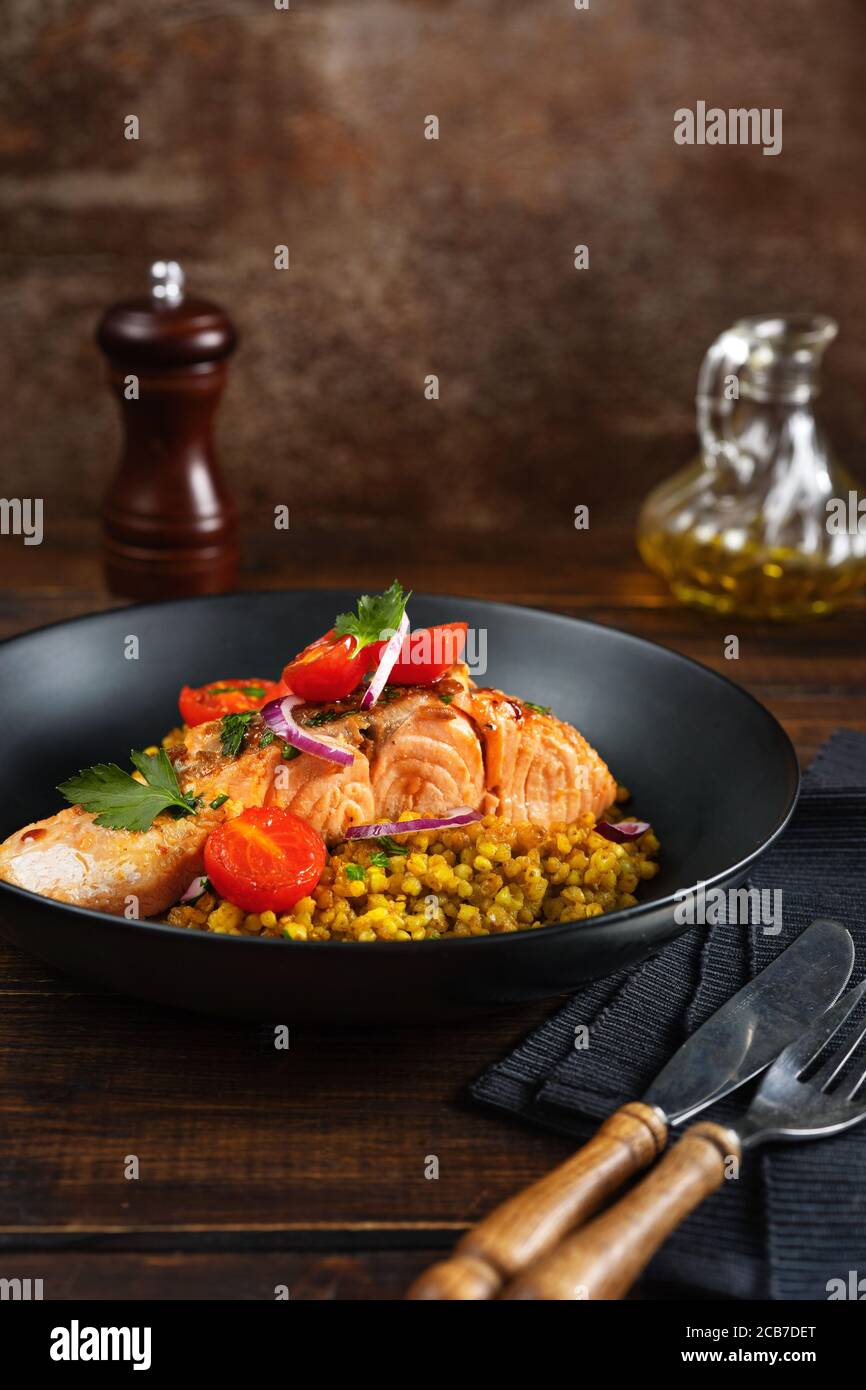 Gros plan du filet de saumon cuit avec les légumes et le sarrasin dans une plaque noire Banque D'Images