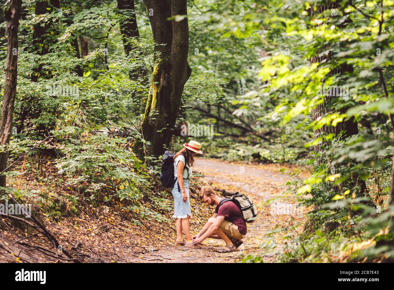 Le jeune homme caucasien avec la barbe prend soin de sa femme, nouant les  lacets sur ses chaussures tout en marchant dans la forêt le long du chemin.  Couple de randonneurs avec