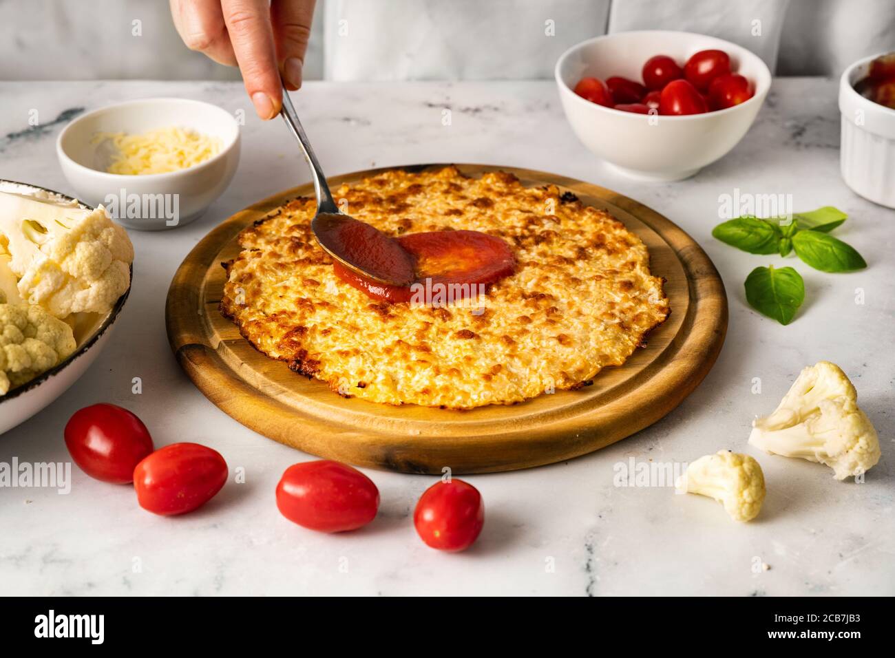 Les mains de la femme se matraque une sauce tomate sur le dessus de croûte de pizza au chou-fleur Banque D'Images