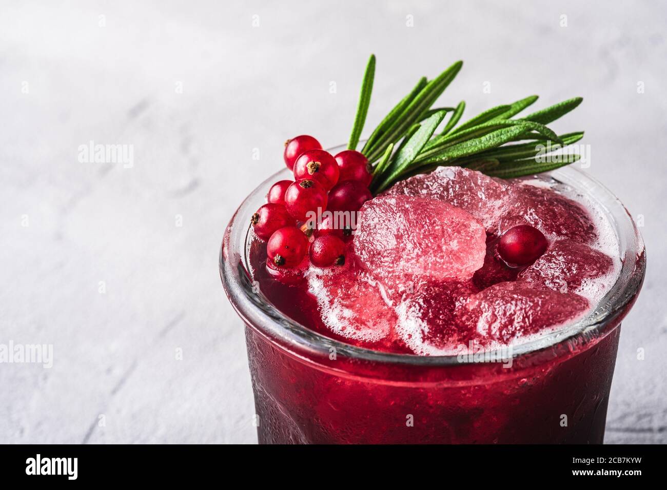 Glace fraîche cocktail de fruits frais en verre, rafraîchissement de cassis rouge d'été avec feuille de romarin sur fond de béton de pierre, vue d'angle macro Banque D'Images